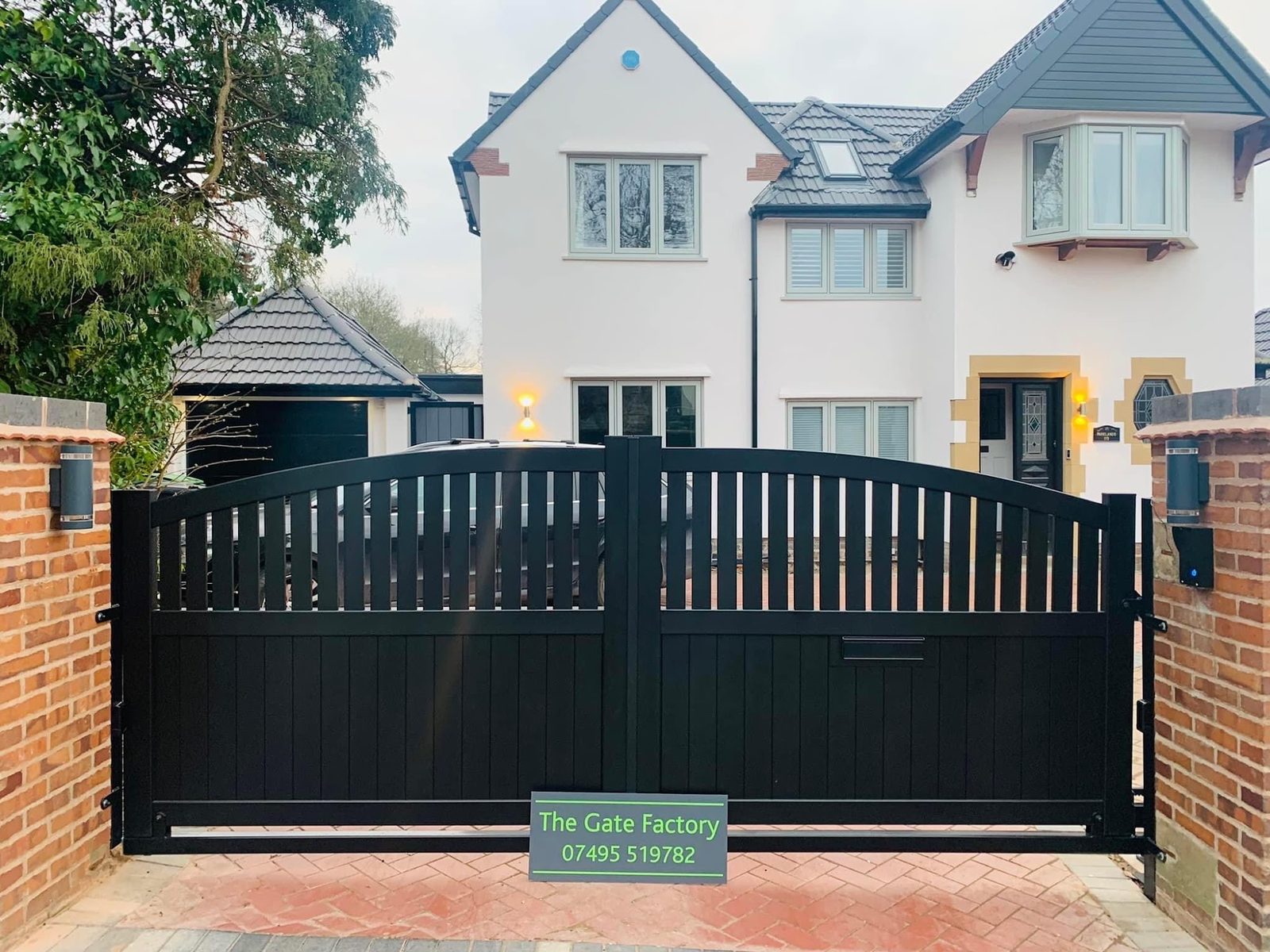 Black arched driveway gates hung between brick piers