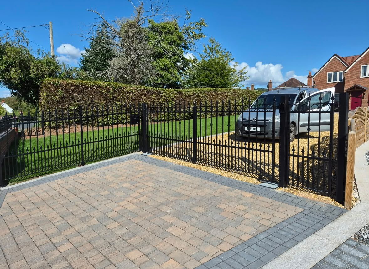 Black spear top railings and matching driveway gates around a block paved drive
